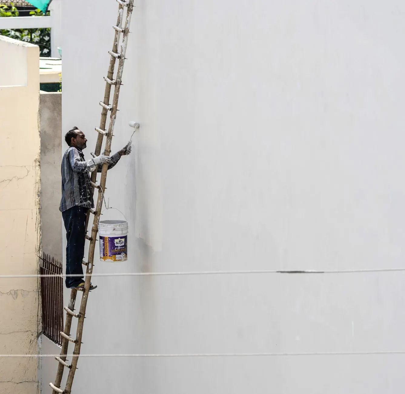 Exterior painting in Marietta, GA: painter on a ladder rolling paint onto an exterior wall